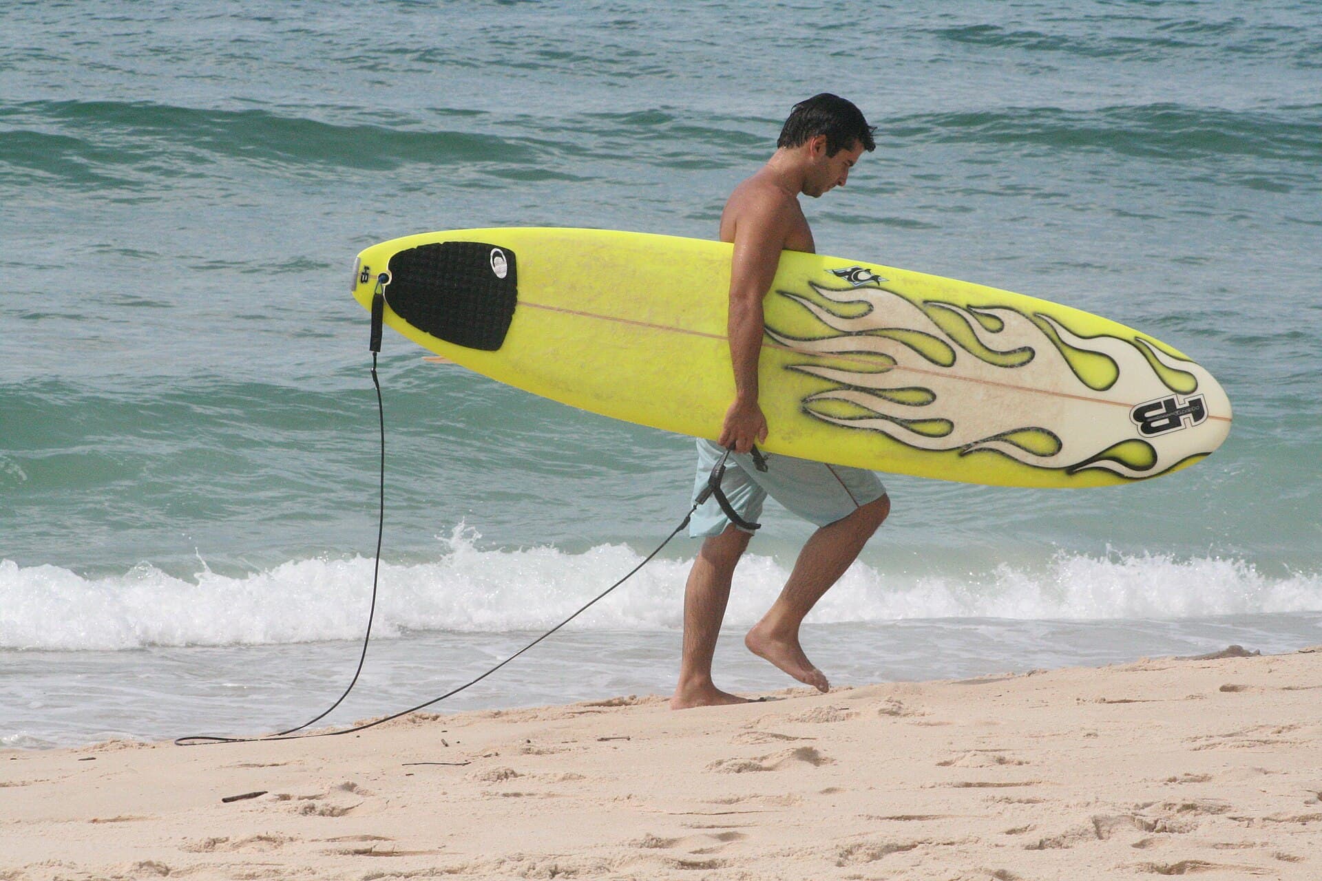 Surfer carrying a longboard along the beach